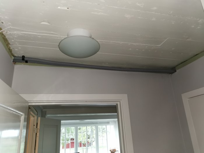 Utsikt av ett rum under renovering med en ojämn vitmålad takyta och utanpåliggande rör längs en kant.