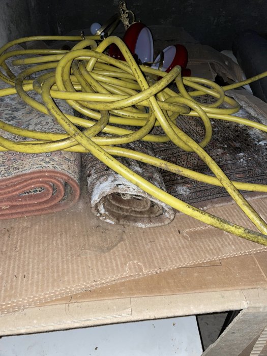 Gul byggelektrisk kabel slängd ovanpå gamla mattor och papp i en rörig miljö.