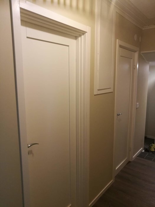 Nyrenoverad korridor med släta vita dörrar och detaljerade dörröverstycken.