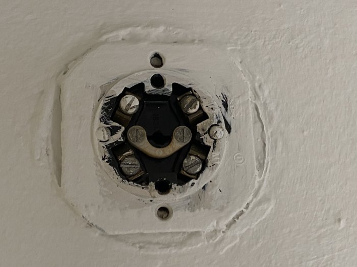 Ett eluttag under installation med öppen kabelanslutning och skruvar mot en vit vägg.