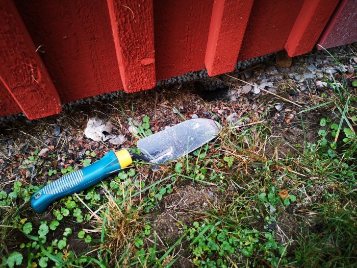 Spade vid grus under röd byggnad med hål grävda av möjligt djur.