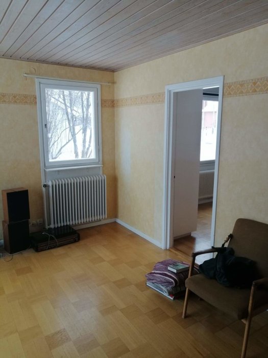 Renovering av vardagsrum från 50-talet med trägolv, ljusa tapeter, fönster och radiator.