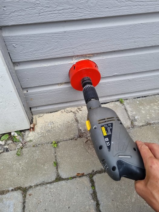 Hålsåg används för att skapa ventilationshål i grått trävägg på ett hus, med verktyget i användarens hand.