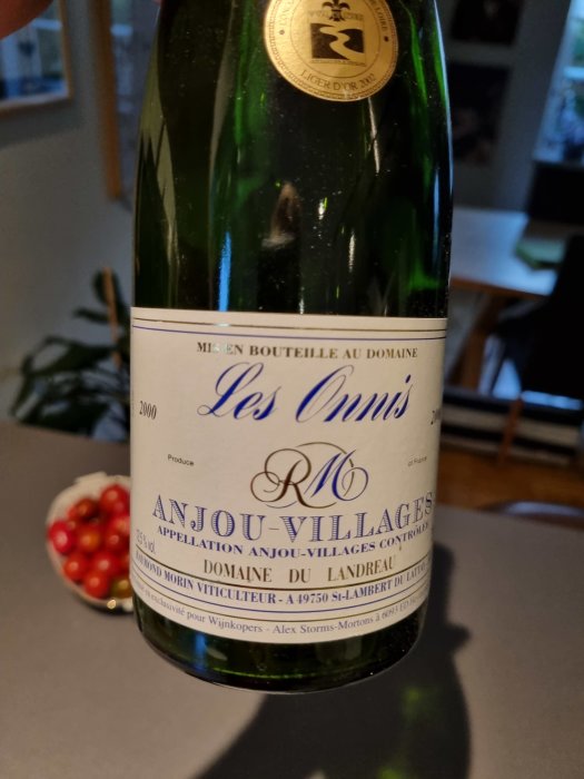 Flaska med Anjou-Villages vin "Les Ondines" årgång 2000 på ett bord, med röda bär i bakgrunden.