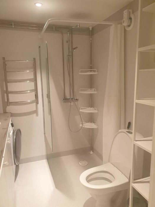 Nyrenoverat badrum med dusch, toalett, tvättmaskin och förvaringshyllor i vitt.