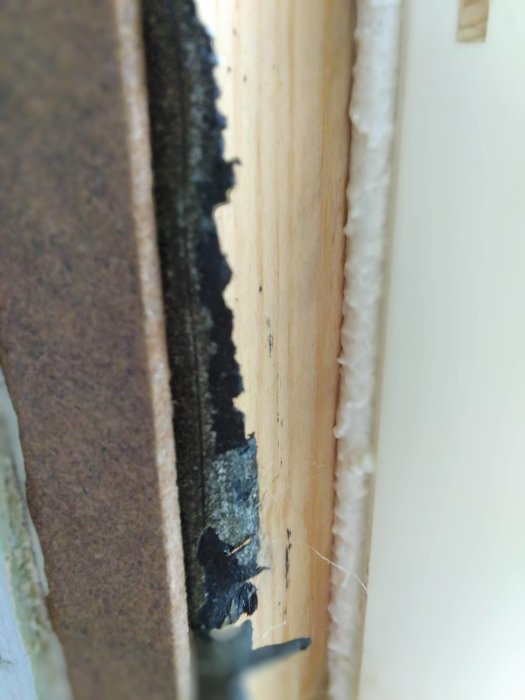 Närbild på en vägg där gipsskiva, reglar och isolering är delvis exponerade.