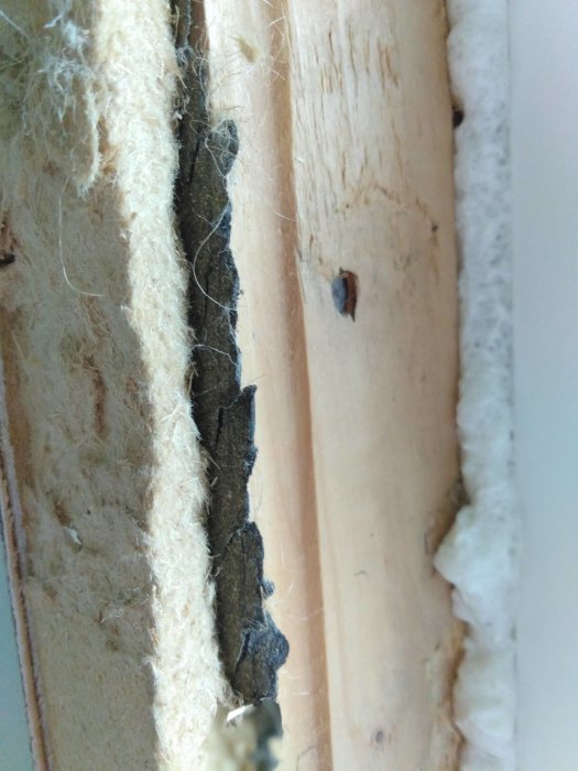 Närbild på en skarv i en träkonstruktion med synliga isoleringsmaterial och tecken på slitage.