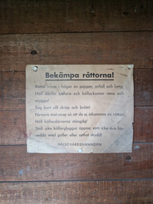 Slitet papper med texten "Bekämpa råttorna!" fäst på en grov, träfärgad dörr, med instruktioner för att hålla källaren ren.