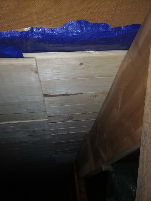 Tätning med blå tejp längs kanten där en trävägg möter taket i ett byggprojekt i ett oisolerat utrymme.
