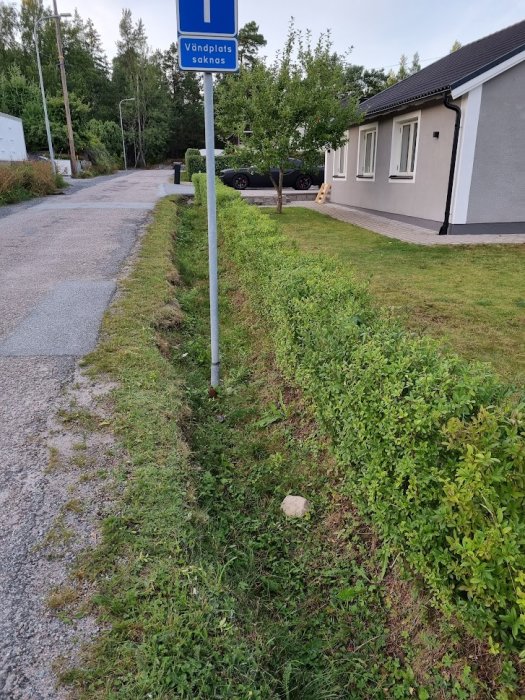 Vägskylt med texten 'Vändplats saknas' vid en gata nära en bebyggelse med hus och parkerad bil.