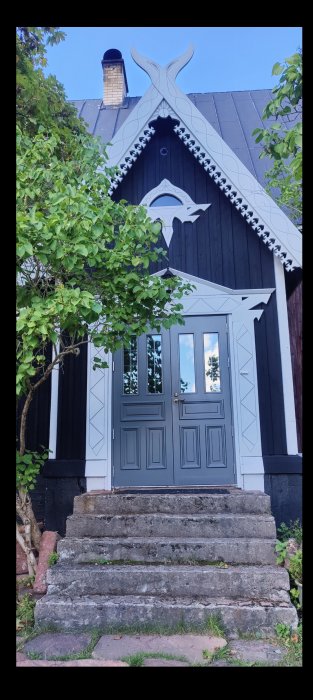 Entré till hus med mörkgrå dörr och vita snickeridetaljer på svartmålad fasad samt stentrappa.