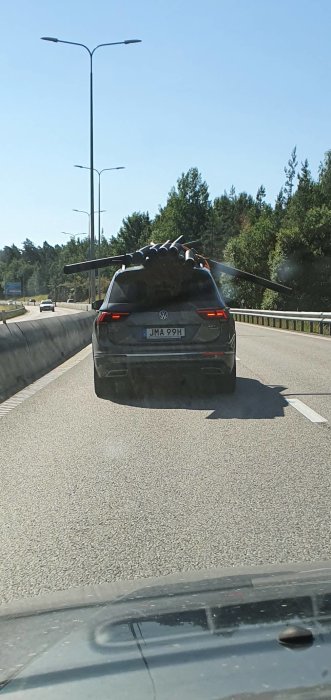 En bil med långa träplankor ohälsosamt utskjutande bakifrån på en motorväg.