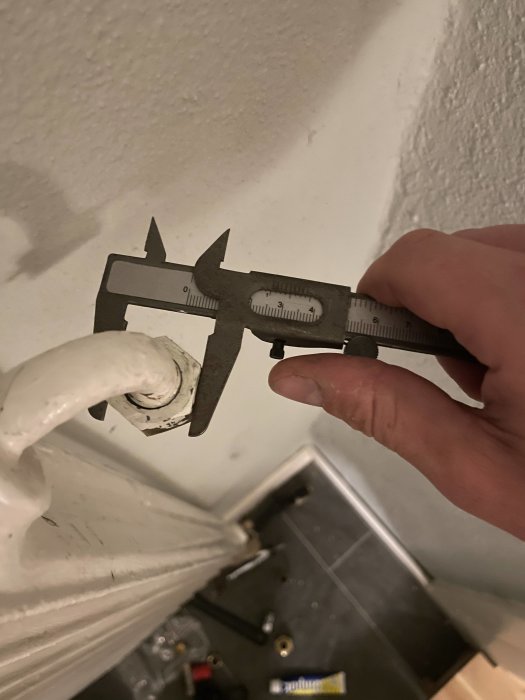 Hand håller ett skjutmått mot en radiatorventil för att mäta dimensioner i en renoveringstråd