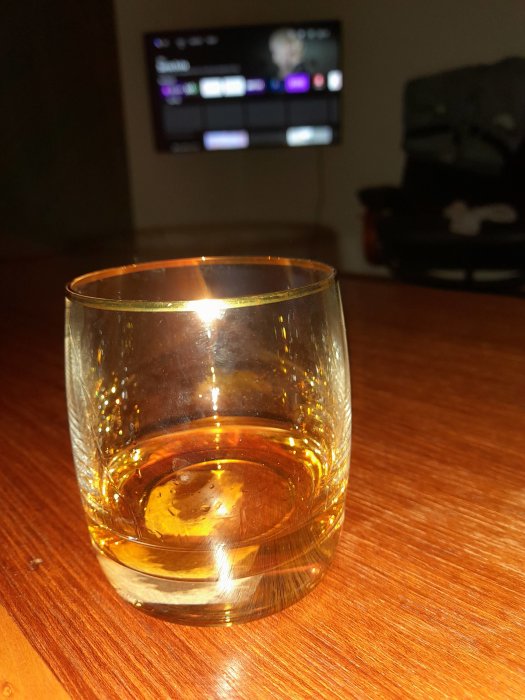 Ett glas med whisky på ett bord framför en suddig TV-skärm.