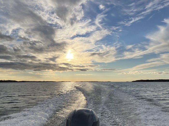 Solsken över havet sett från en båt som skapar vågor i vattnet.