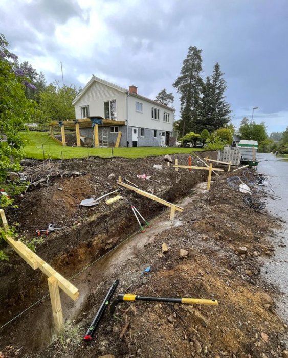 Utgrävning för stödmur med färdigställda formreglar och armeringsjärn framför hus.