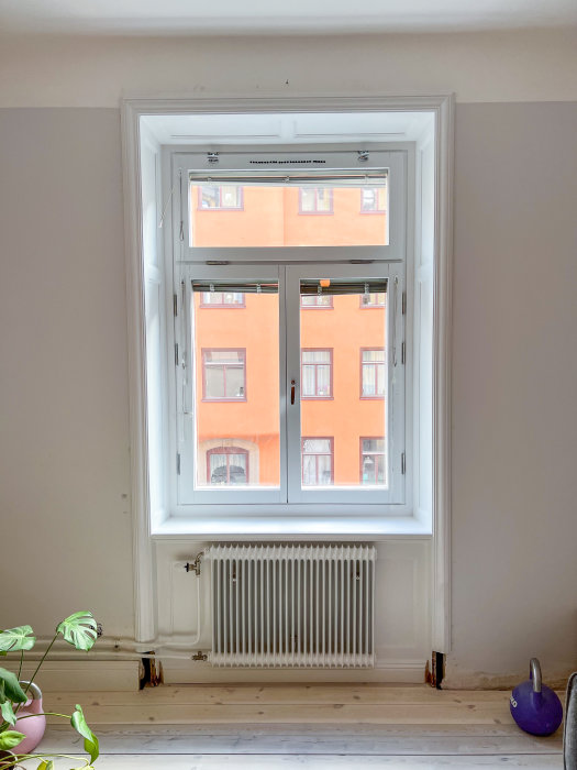 Nyinstallerat fönster med öppningsbara glas och utsikt över orange byggnad, radiator och trägolv syns.