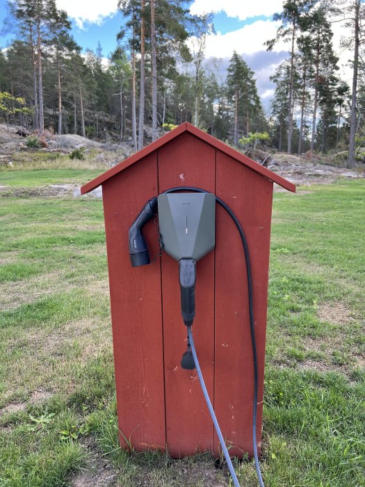 Fristående röd laddstolpe med en installerad laddbox och ansluten kabel utomhus.