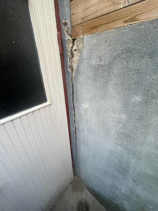 Spricka i hörnet av en byggnad där puts möter träbeklädnad vid ett fönster.