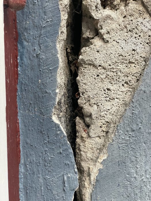 Stor spricka i en grå betongvägg intill blå målad vägg och röd kant.
