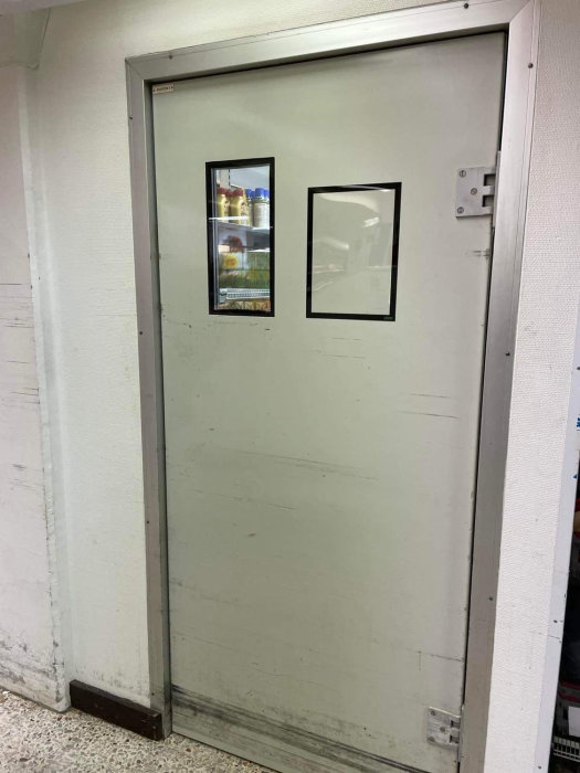 En stängd metall dörr med två fönster, monterat med säkerhetshasp och ljus vägg i bakgrunden.