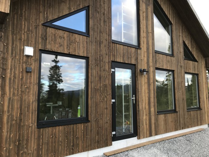 Träfasad med fönster och fasadbelysning på ett nybyggt hus, redo för köksmontage.