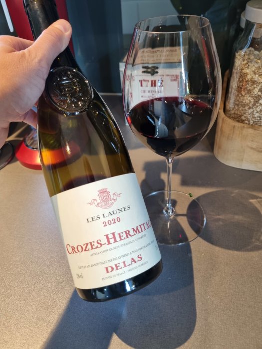 Hand håller en flaska Crozes-Hermitage vin bredvid ett vinglas, på en köksbänk.