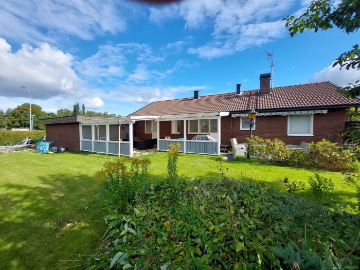 Ett egnahemshus med tegeltak, förlängd veranda och en grön gräsmatta.