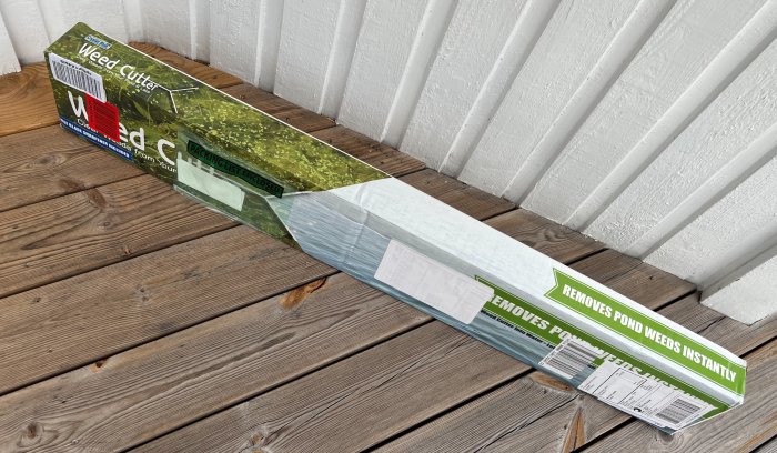 En förpackning av ogräsborttagaren "Weed Cutter" på ett trägolv intill en vit vägg.