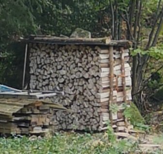 Vedstapel med kluvna grenar i olika storlekar under ett enkelt skydd av plankor.