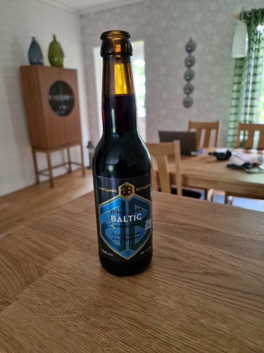 Flaska Jämtlands Baltic Imperial Stout på träbord med suddig bakgrund av ett vardagsrum.