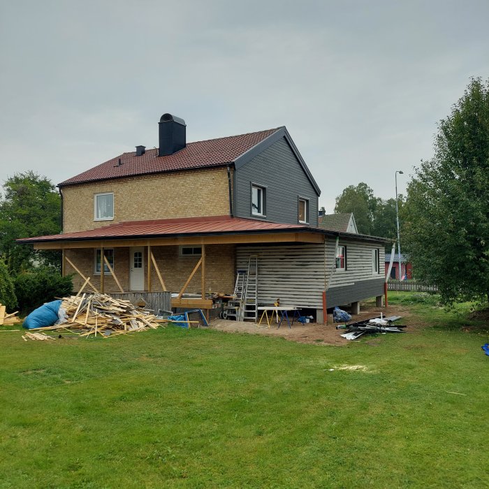 Ett hus under renovering med nytt aluminiumtak och byggmaterial utspridda på gräsmattan.