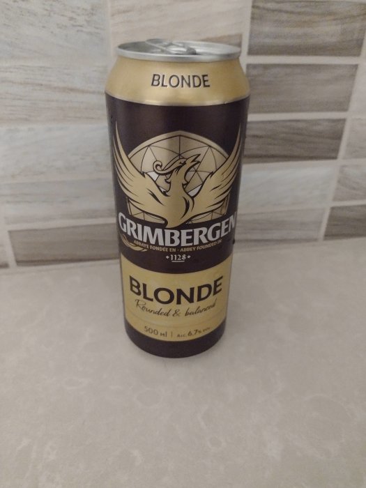 En burk Grimbergen Blonde öl med beskrivning på estniska mot kakelbakgrund.