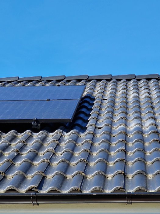 Solpaneler som delvis täcker takpannor på ett hustak mot klarblå himmel.