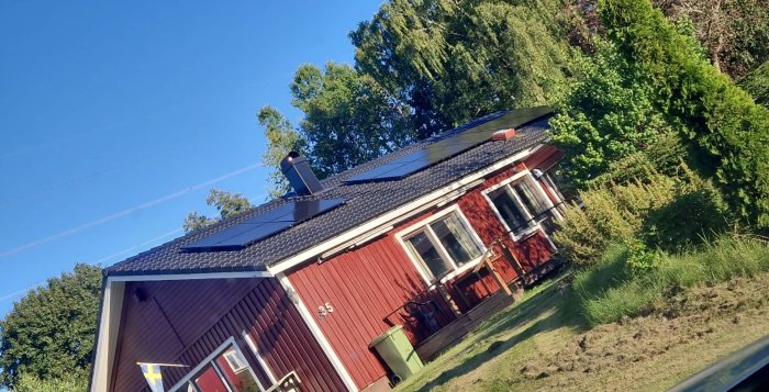 Solpaneler installerade på båda sidor av ett rött hus med svart tak, nära en ventilationstakhuv.