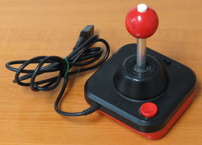 Retro joystick med röd kulspak, en knapp och kabel, förlagd på ett träbord.