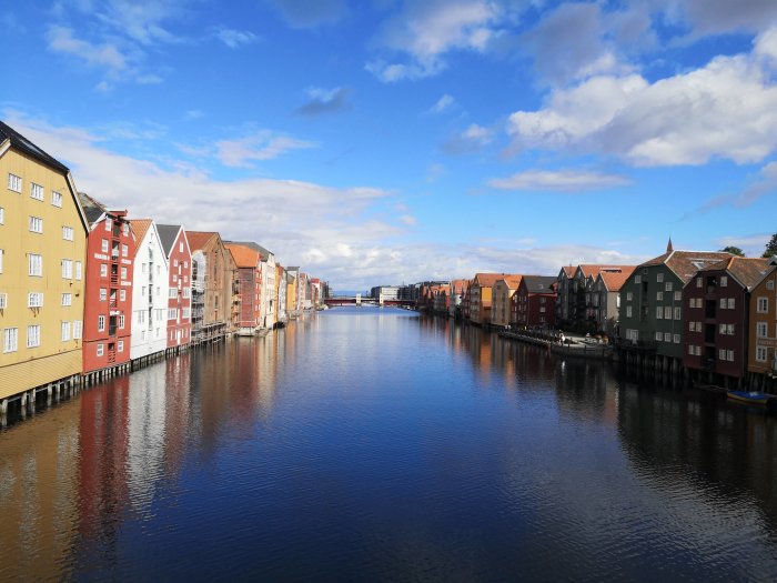 Färgglada trähus längs Nidelven i Trondheim under en klar himmel.