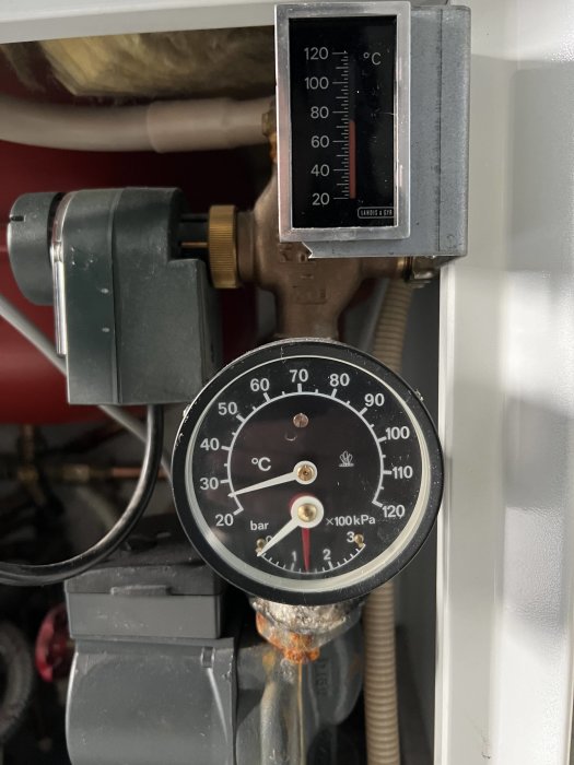 Termometer och manometer monterade på rörsystem, visar temperatur och tryck.