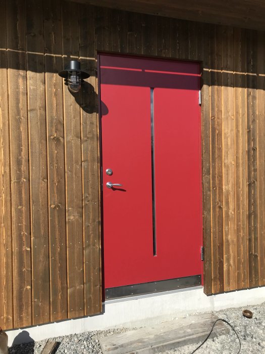 Nyinstallerad röd ytterdörr på hus med träsidor, omgiven av byggmaterial.