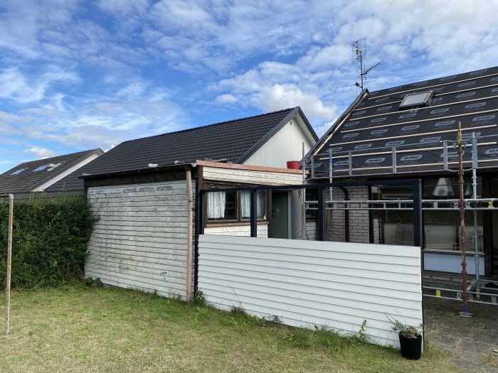 Hus med ställningar och renovering pågår, täckt tak och en del av trädgården syns.