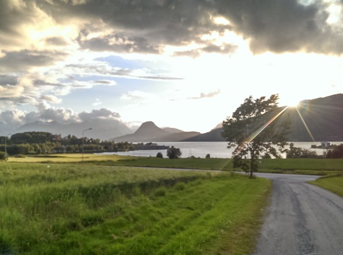 Solnedgång över en landsväg med utsikt över sjö och berg.