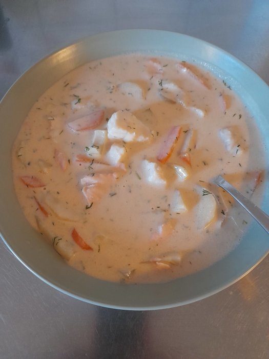 En skål med fisksoppa med bitar av torsk som faller sönder, dill och morötter.