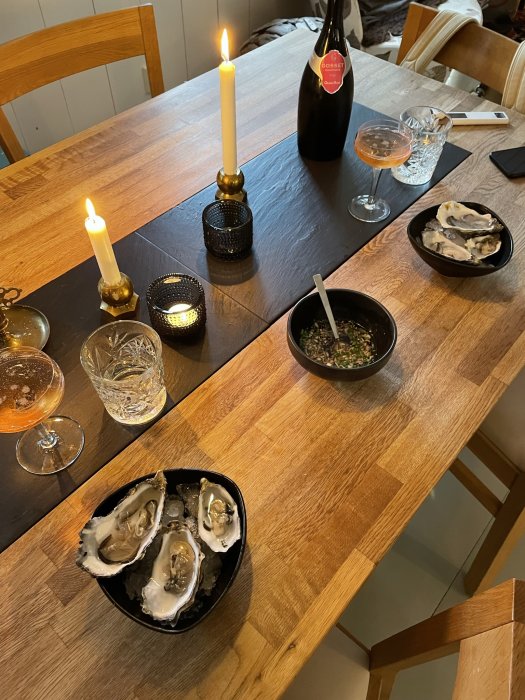 Ett bord dukat för förrätt med tända ljus, en flaska champagne, glas och en skål med ostron.