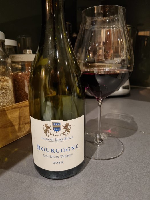 Flaska Bourgogne-rödvin med etikett "Les Deux Terres 2019" bredvid ett glas med vin.