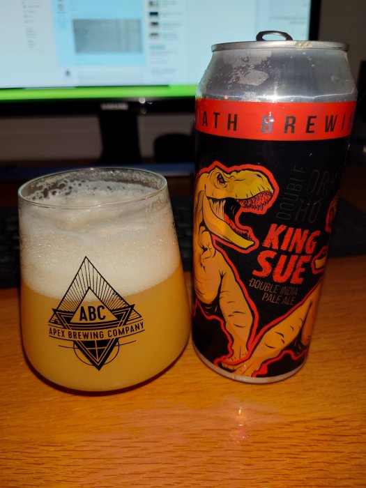 Ölburk med King Sue-illustration bredvid ett glas öl framför datorskärm.