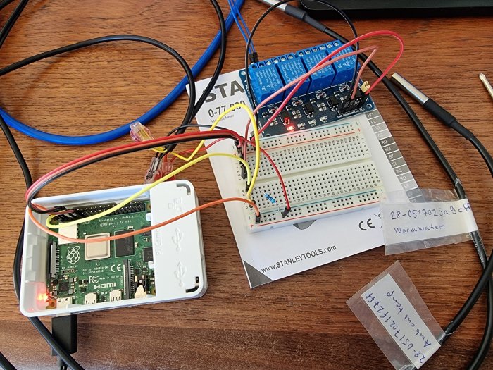 Elektronikprojekt med en Raspberry Pi och reläkort kopplade till en breadboard med kablar och temperatursensorer.