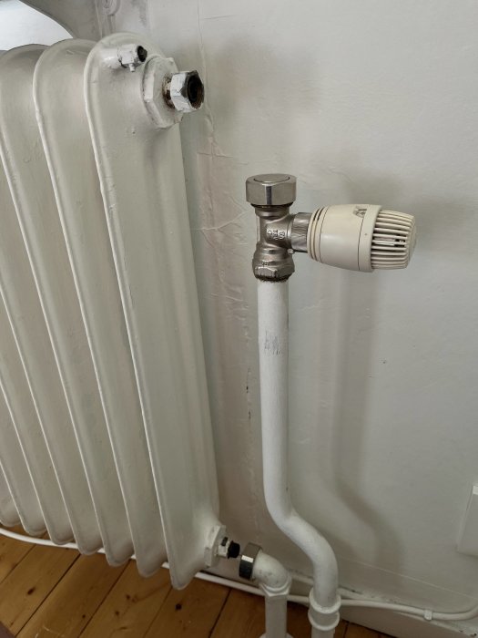 Vit radiator med termostatventil och anslutna rör mot en vit vägg.