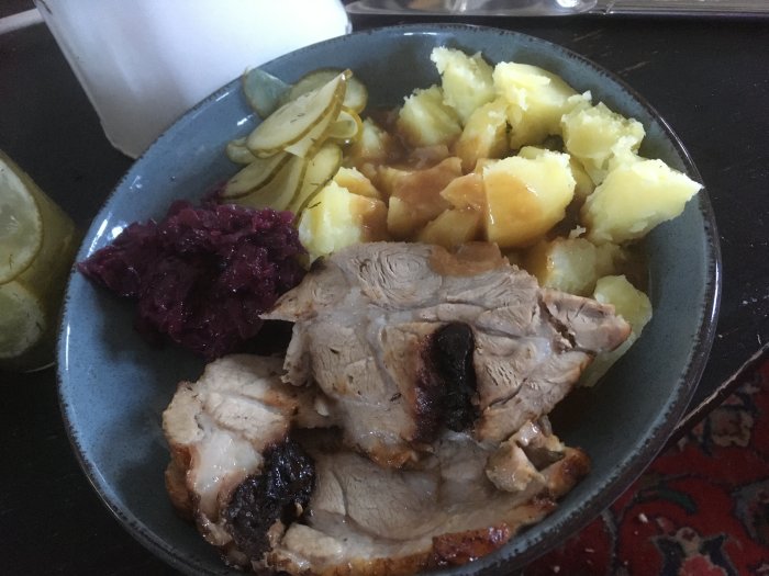 Plommonspäckad fläskkarré med potatis, rödkål och inlagd gurka på en tallrik.