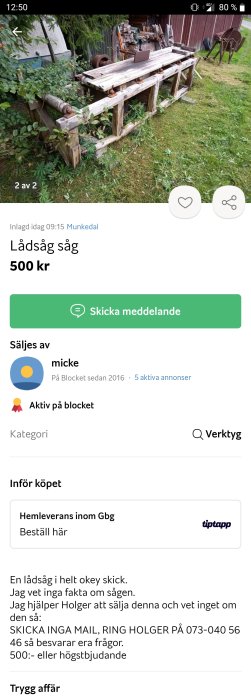 En gammal bandsåg till salu för 500 kr, placeras utomhus omgiven av vegetation och annat träverk.