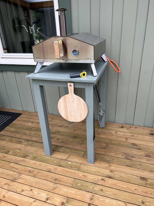 Pizzaugn från Austin BBQ placerad på ett grått bord utomhus med träspade och termometer vid sidan.